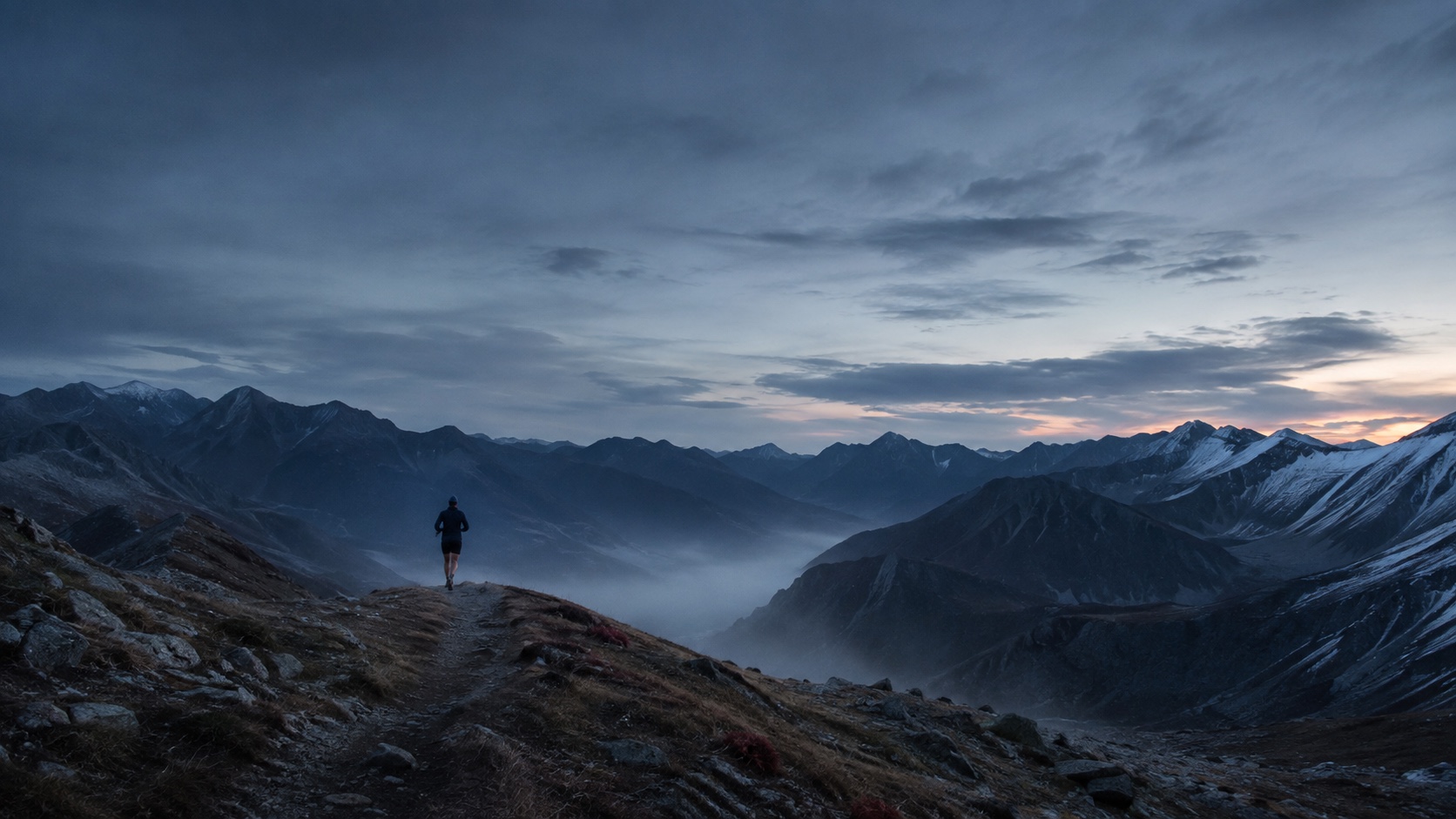 Ein Läufer auf einem Bergpfad vor weitem Alpenpanorama im ersten Morgenlicht